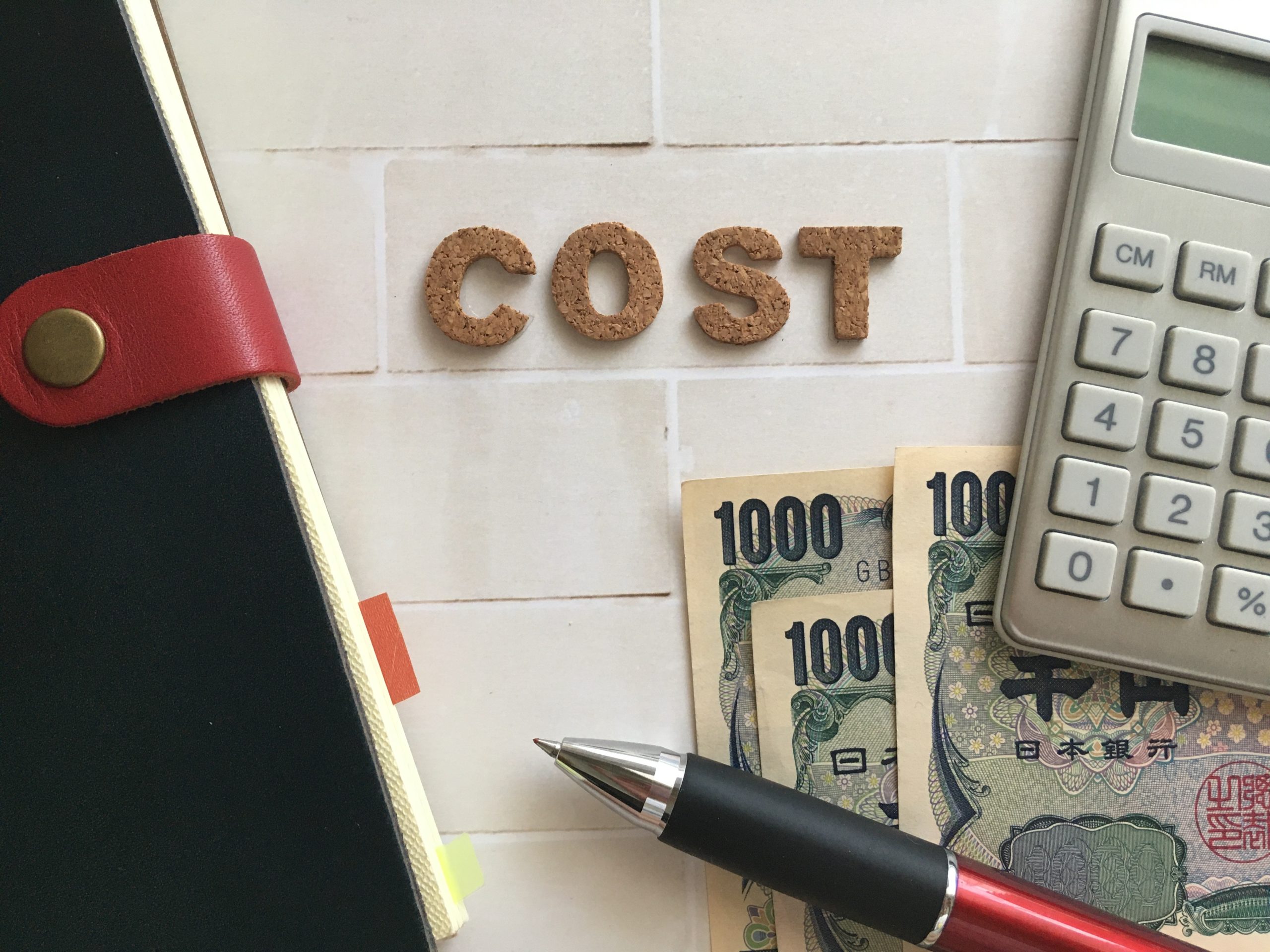 タイルにCOSTというコルク材が貼ってあるのと、3千円と手帳と電卓とボールペンが写ってるイメージ