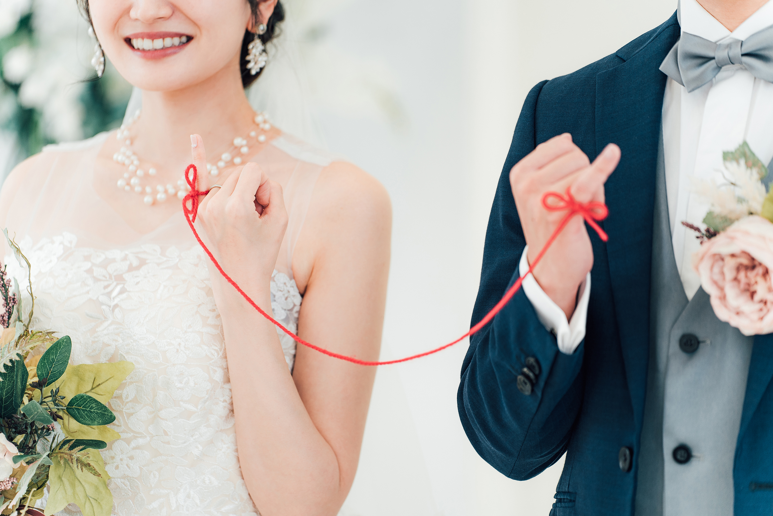 結婚式場で赤い糸で結ばれる新郎新婦の写真