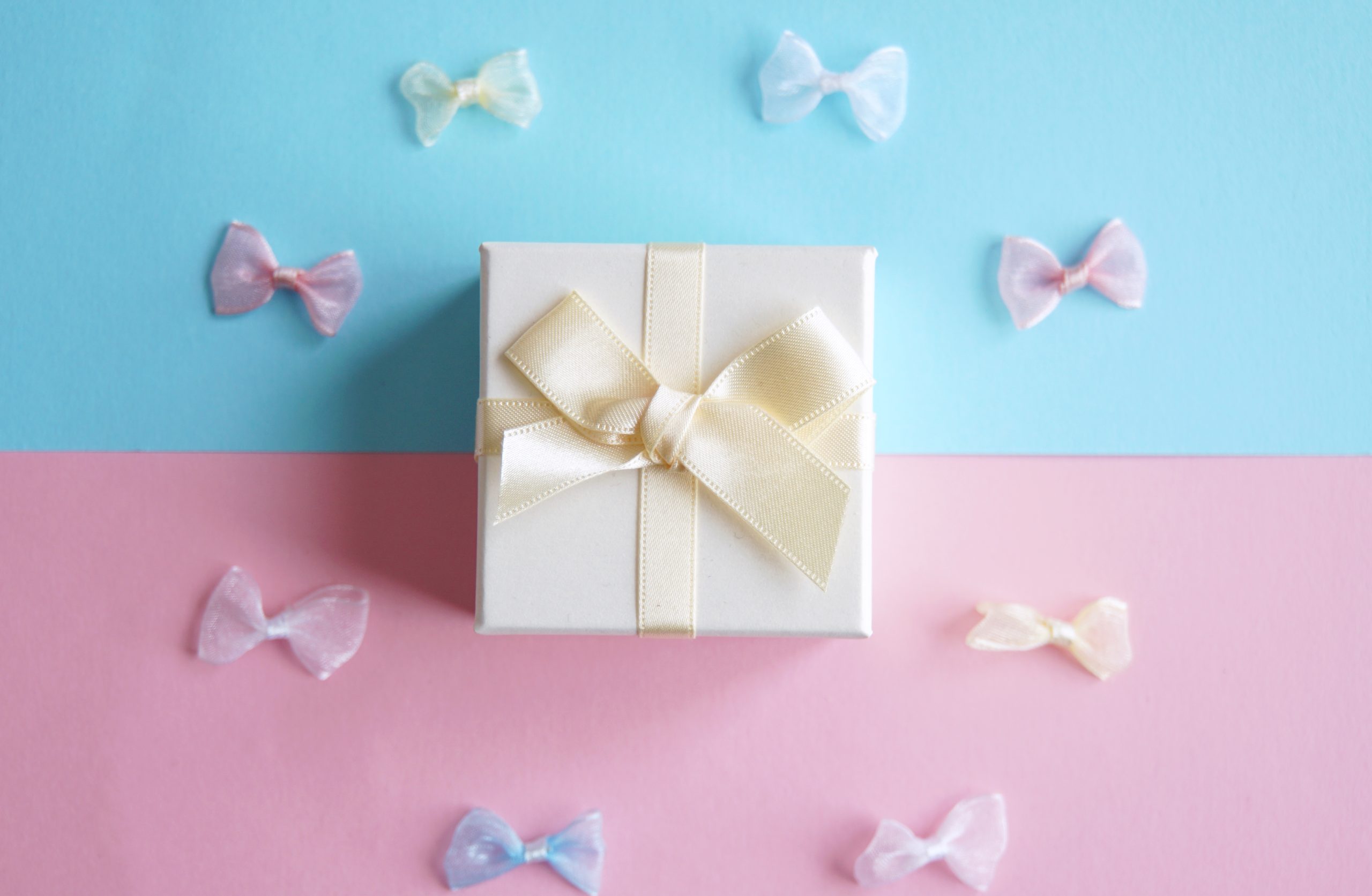 水色とピンクの背景に白いプレゼントボックスとリボンがうつってるイメージ