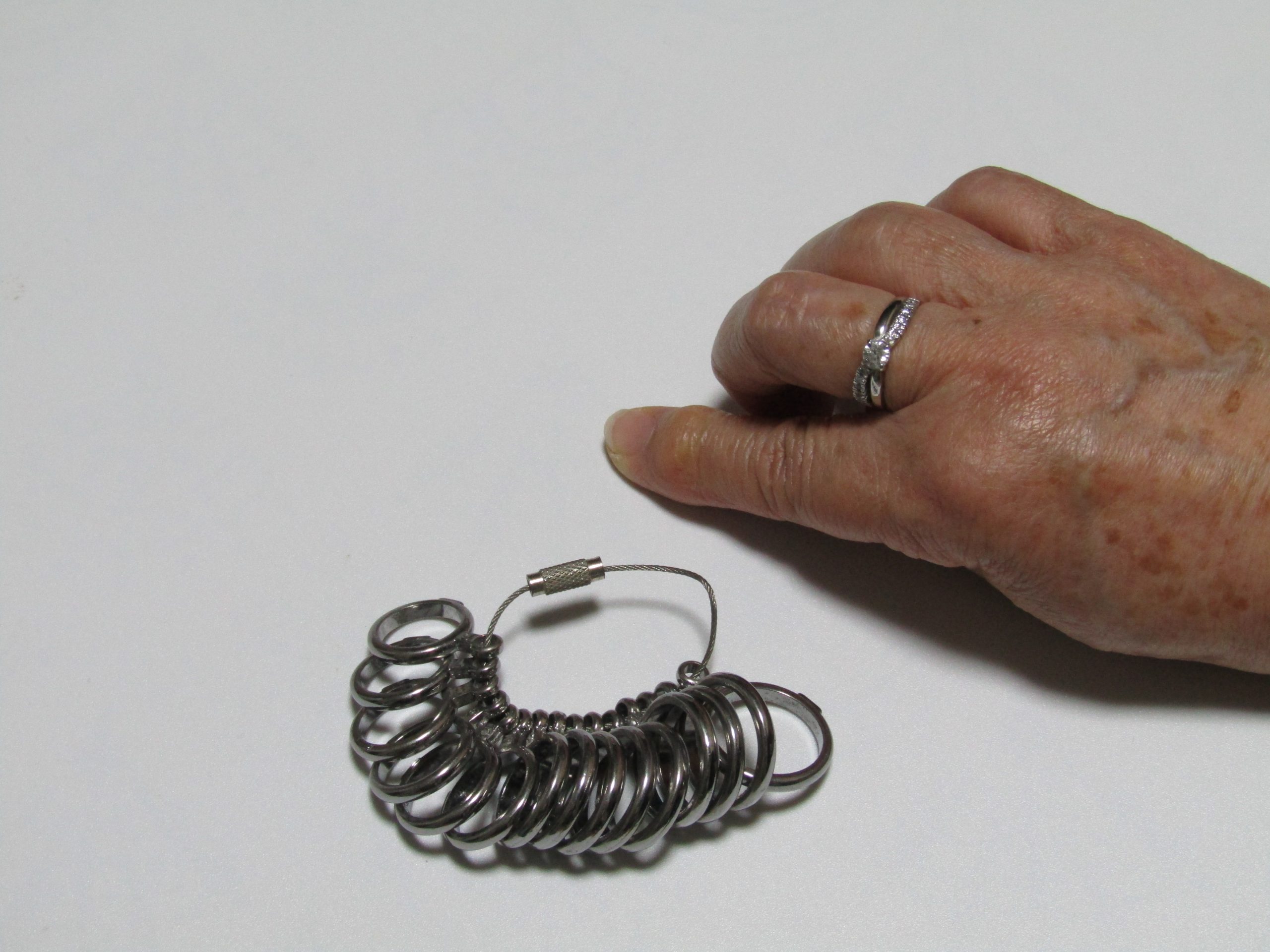 指のサイズを測るための道具［リングゲージ］と指輪をしている女性の手の写真